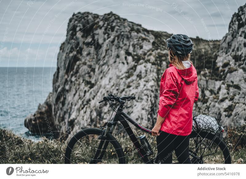 Anonymous female bicyclist on rocks woman bicycle cliff helmet sea landscape unrecognizable extreme young person cheerful active walking lifestyle ride bike