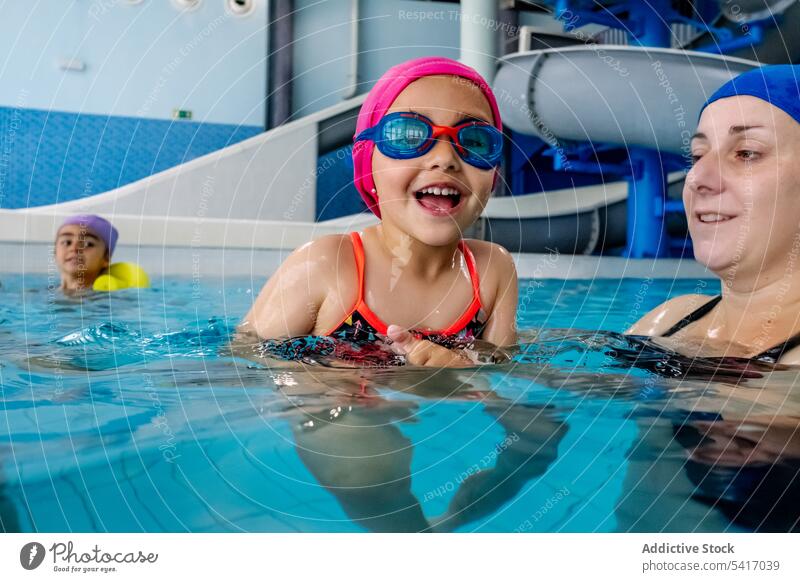 Cheerful girl swimming in pool with mother water park excited fun weekend together amusement woman kid child goggles hat cheerful happy resort family daughter