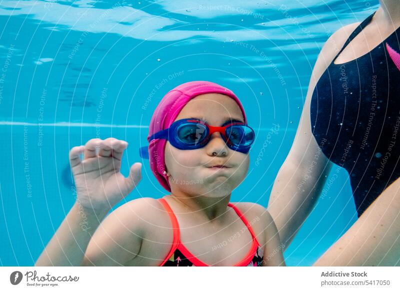 Cheerful girl underwater swimming in pool with mother park excited fun weekend together amusement woman kid child goggles hat cheerful happy resort family