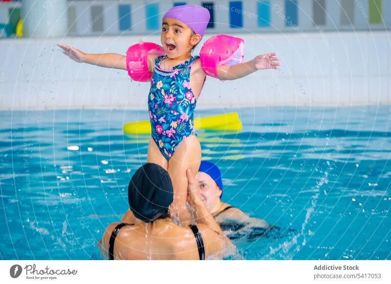 Mother playing with daughter in swimming pool mother fun water lifting outstretched arms ethnic together family parent woman girl kid child cheerful happy
