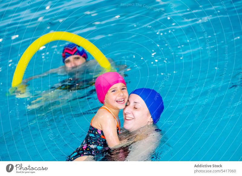 Cheerful girl swimming in pool with mother water park excited fun weekend together amusement woman kid child goggles hat cheerful happy resort family daughter