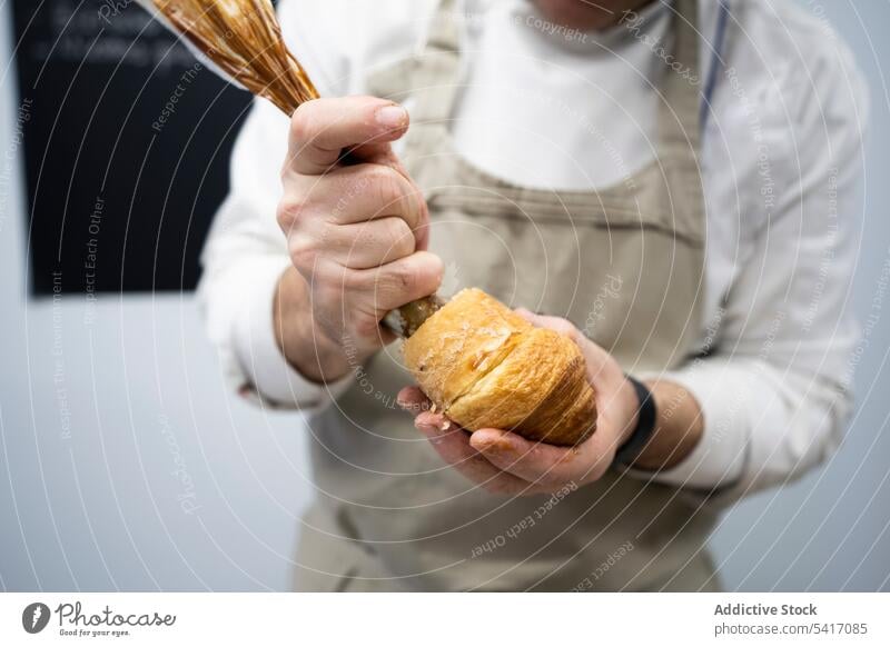 Confectioner pouring chocolate filling into croissant man stuffing cream dessert confectioner chef cake cook occupation work piping bag pastry male adult person