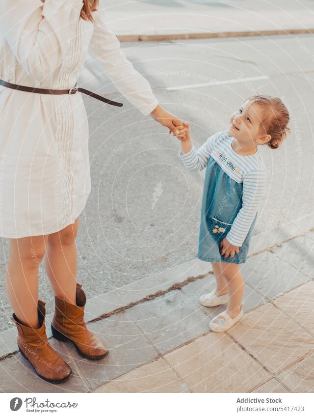 Mother and daughter standing on street mother city sidewalk holding hands family together sky cloudless blue woman girl kid child mom parent pavement town