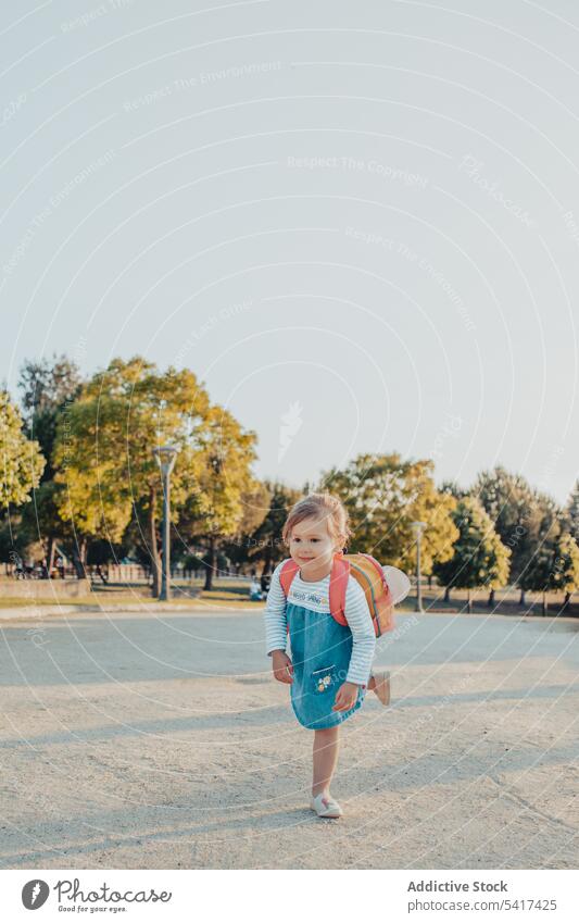 Little girl standing in park smiling little sand lifestyle leisure backpack casual happy kid child sunny daytime weekend rest relax summer preschooler stylish
