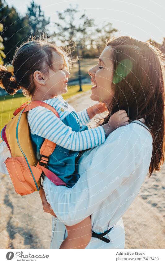 Mother kissing daughter in park mother sunny daytime embracing carrying lifestyle leisure together woman girl kid child backpack rest relax weekend family