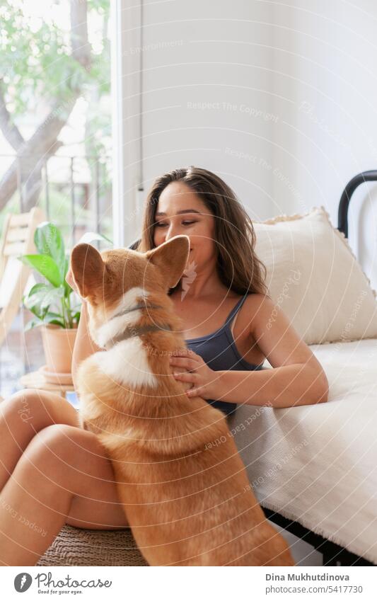 millennial caucasian woman at home with corgi dog. Dog owner and trainer. Funny cozy picture of female with puppy in apartment. Brunette smiling with welsh corgi Pembroke dog sitting on couch.