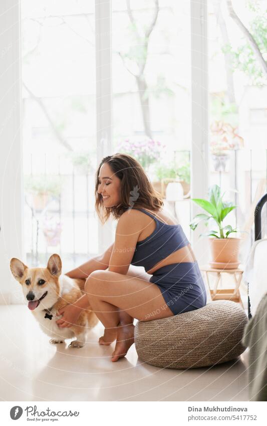millennial caucasian woman at home with corgi dog. Dog trainer. Funny cozy picture of female with puppy in apartment. Brunette smiling with welsh corgi Pembroke dog sitting on couch.