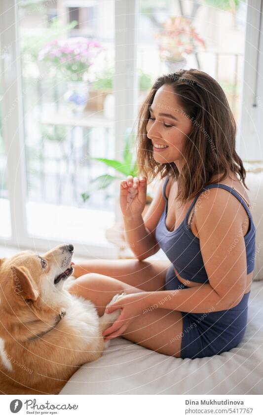 millennial caucasian woman at home with corgi dog. Dog trainer. Funny cozy picture of female with puppy in apartment. Brunette smiling with welsh corgi Pembroke dog sitting on couch.