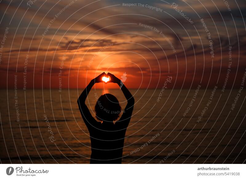 Young woman on rocks forming heart with hands at sunset by sea Sunset Sunlight sunny Summer Summer vacation Summery Summertime Summer feeling Ocean Sea water
