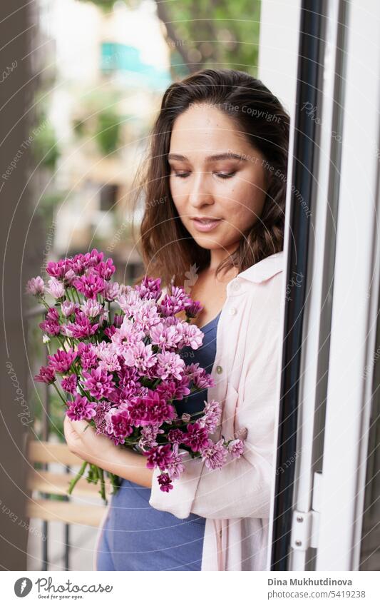 Beautiful woman with flowers bouquet on the balcony. Happy brunette smiling. Plants and flowers gardening hobby. Balcony plant Balcony furnishings Summer