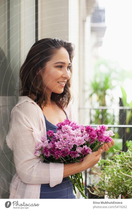 Beautiful woman with flowers bouquet on the balcony. Happy brunette smiling. Plants and flowers gardening hobby. Balcony plant Balcony furnishings Summer