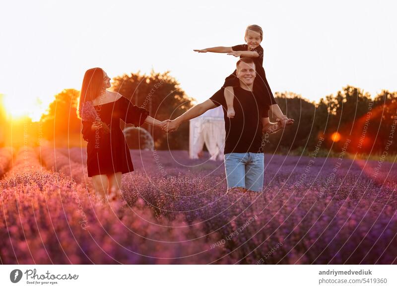 happy family day. Young mother and father carrying on shoulders daughter in lavender field on sunset. Dad, mom and child girl having fun on nature on summer. Concept of friendly family. family look