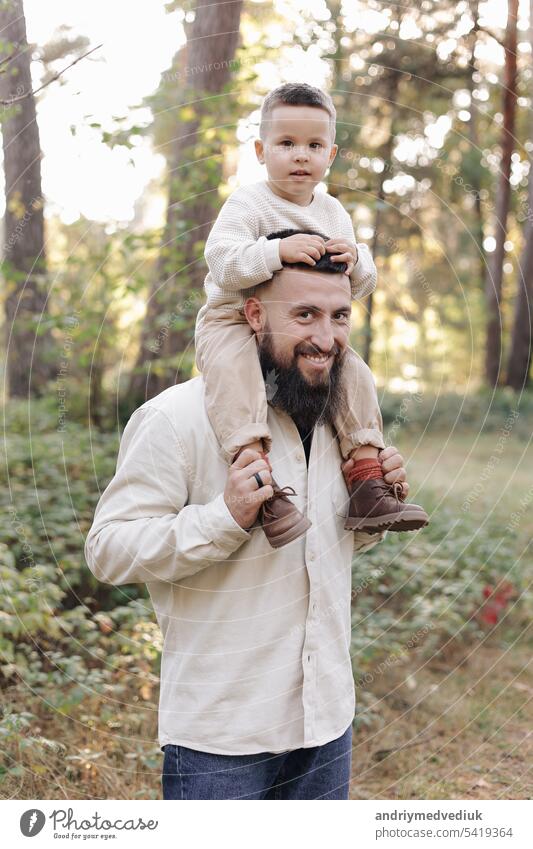 Father's day. Smiling dad holding his toddler son on shoulders look at camera outdoor at nature. Family spend and enjoy time together. Happy fatherhood and childhood, family love, togetherness concept