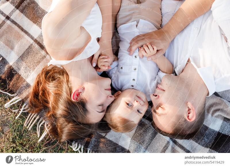 Mom, dad and little son lying on the blanket in the summer park. The concept of summer holiday. Mother's, father's, baby's day. Family spending time together on nature. Family look