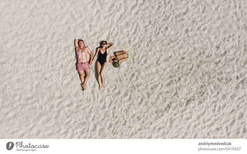 Aerial view of a young couple lying on the white beach sand. man and woman in swimwear spend time together and travel through the desert aerial vacation