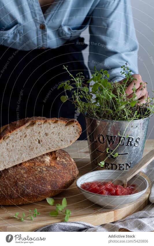 Anonymous woman touching plant near bread cooking sourdough preparing sandwich open red sauce kitchen spoon green meal food lunch breakfast morning lifestyle