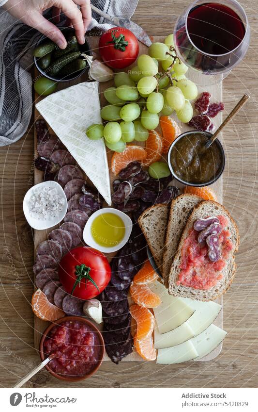Anonymous person eating delicious snacks for wine tray fruits red glass vegetable meat sausage slice tomato sauce open sandwich melon tangerine grape cheese
