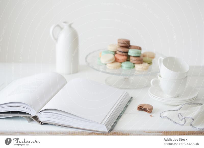 Macaroons on white table with book and crockery macaroon cup dessert sweet set page composition tea tasty food delicious colorful gentle design morning