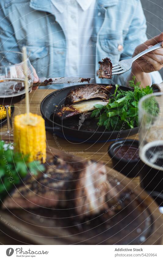 Person eating grilled meat in restaurant corn steak person herb green roast tasty bone barbecue rustic wooden food meal delicious cook vegetable dinner dish
