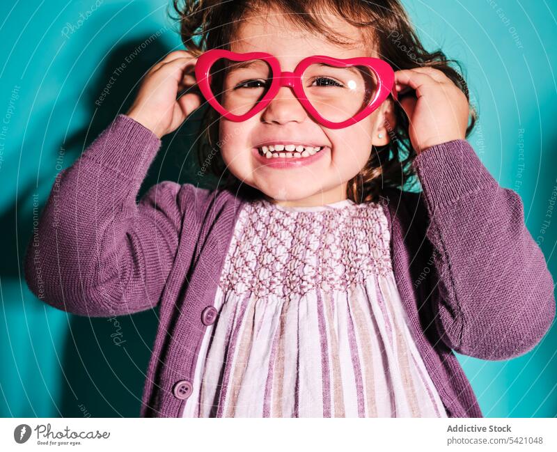 Playful preschooler in hear shape glasses child girl kid playful rainbow happy woman positive style cheerful accessory dress joy toothy smile cute small female
