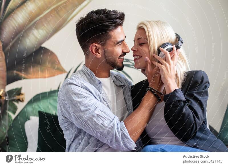 Happy couple listening to music together smile love kiss diverse headphones man woman happy share flirt home relationship girlfriend boyfriend affection feeling