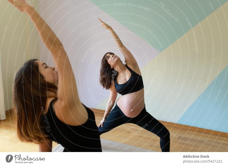 Pregnant woman doing yoga with trainer women studio pregnant reverse warrior pose repeat training exercise together healthy wellness practice well-being belly