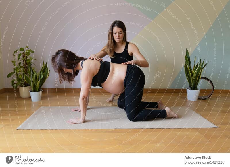 Female instructor supporting pregnant woman during yoga training women studio trainer box pose exercise together healthy wellness practice well-being belly