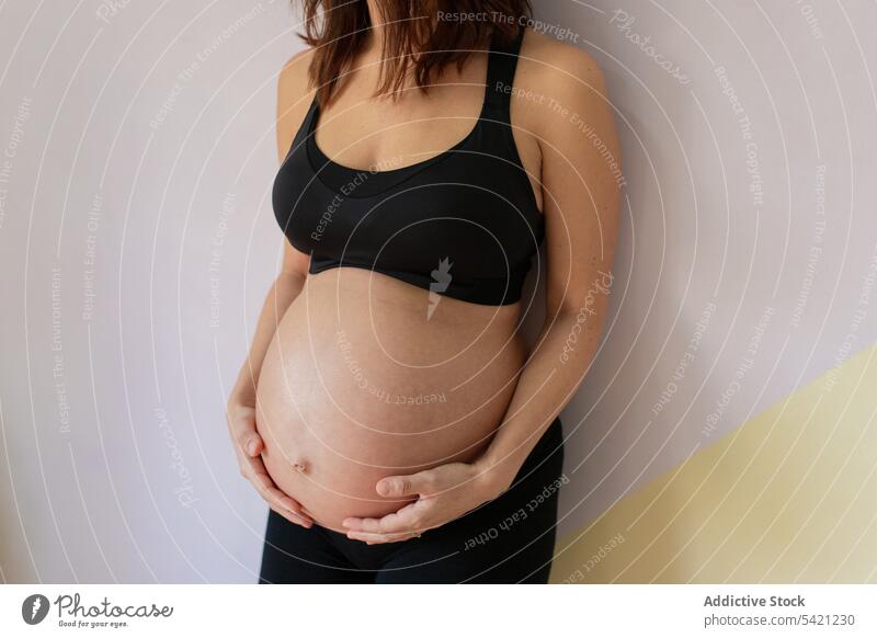 Crop pregnant woman near wall in yoga studio break touch belly lean training female sportswear healthy wellness well-being tummy expect relax rest maternal calm