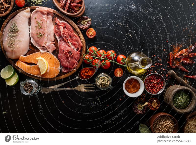 Flat lay of proteins surrounded by spices and seasonings on table product meat salmon condiment fish fillet food pepper cutting board spoon aromatic assorted