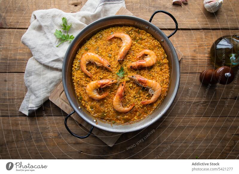 Large pan of savory rice dish with aromatic yummy fried prawns on wooden table paella shrimp towel roasted food rustic culinary homemade nutrition fresh