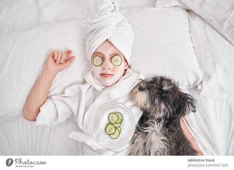 Kid with facial mask lying on bed with dog kid cucumber beauty skin care relax enjoy spa natural funny child fresh clean cosmetology therapy pet animal