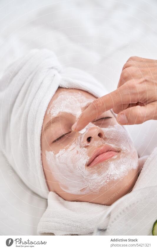 Woman applying mask on face of kid beauty cucumber skin care spa enjoy procedure treat facial relax bed natural child fresh clean cosmetology therapy cosmetic