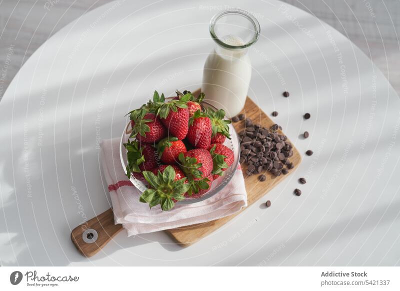 Strawberries and chocolate pellets with milk strawberry morning breakfast table kitchen napkin cutting board ripe heap bottle bowl fruit drink dessert home food