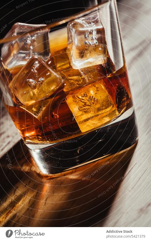 Glass of scotch in rays on aged rustic table in darkness glass whiskey bourbon alcohol beverage ice drink liquid liquor cognac brandy transparent fluid pour