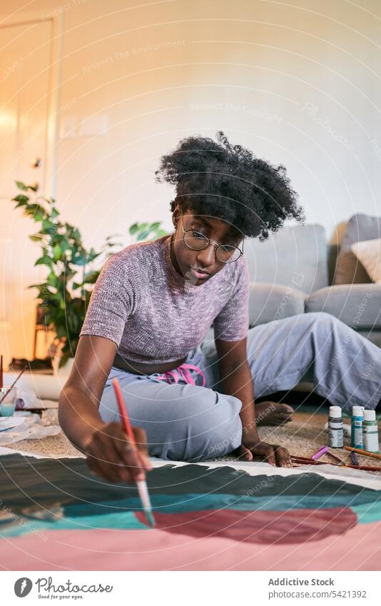 Young African woman drawing picture at home paint brush young casual focus amateur hobby female black free time artist ethnic room paintbrush paper floor