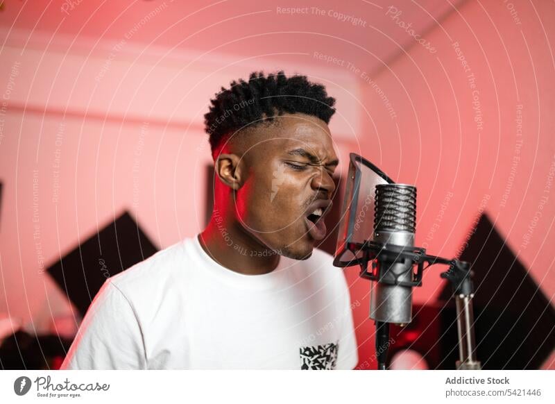 Black musician singing into microphone in studio singer song mouth opened professional enjoy man portrait haircut device t shirt millennial equipment modern