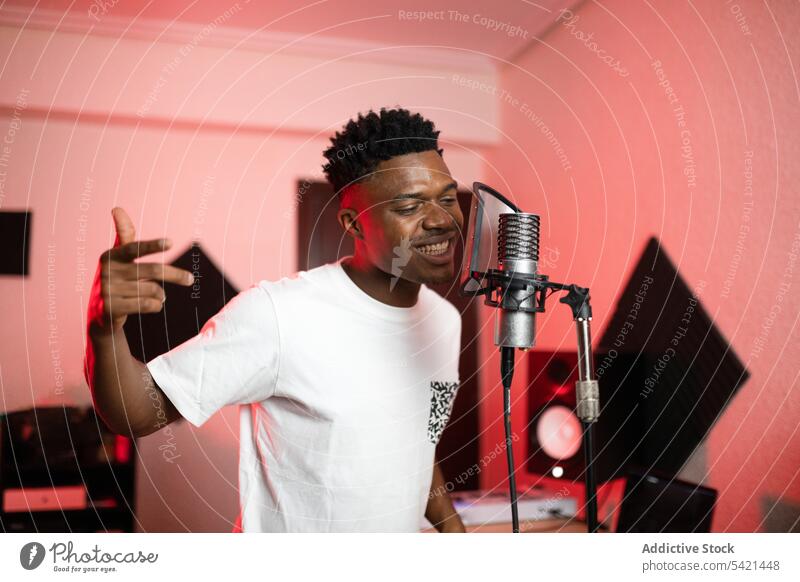 Black musician singing into microphone in studio singer song mouth opened professional enjoy man portrait haircut device t shirt millennial equipment modern