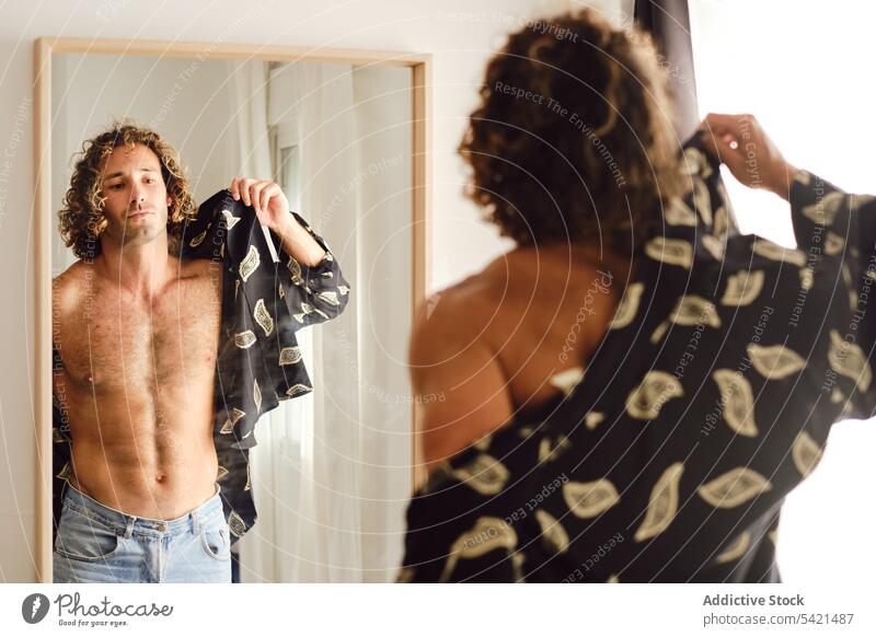 Fit man putting on shirt and looking in mirror put on fit dress up home cloth outfit style male room reflection modern prepare apartment flat stand guy