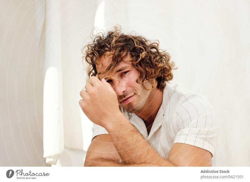 Smiling man with curly hair looking at camera on white background smile handsome appearance delight chair complexion style lean on hand male sit joy casual glad