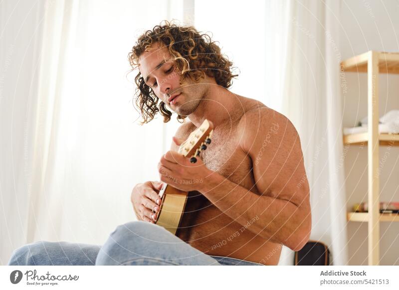 Shirtless man playing ukulele on bed at home music musician naked torso handsome hobby instrument male relax sit harmony peaceful practice entertain sound