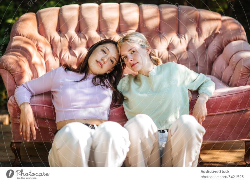 Delicate teenage sisters sitting near sofa in garden tender sibling bonding charming serene relax rest together couch friend friendship friendly delicate gentle
