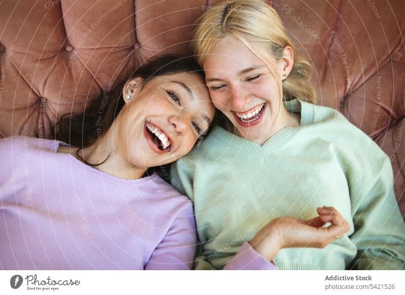 Delighted teen sisters lying on sofa and laughing teenage having fun cheerful together bonding chill entertain weekend happy content couch rest relax friendship