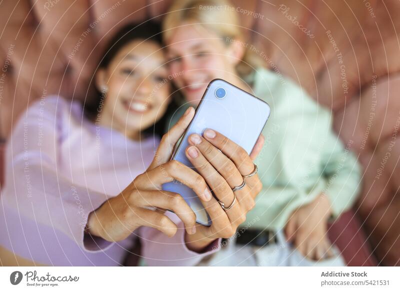 Content teenage sisters taking selfie on smartphone on couch self portrait girl mobile tender young sofa using lying device smile delicate gentle delight
