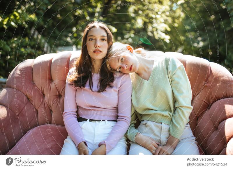Delicate teenage sisters sitting on sofa in garden tender sibling bonding charming serene relax rest together couch friend friendship friendly delicate gentle