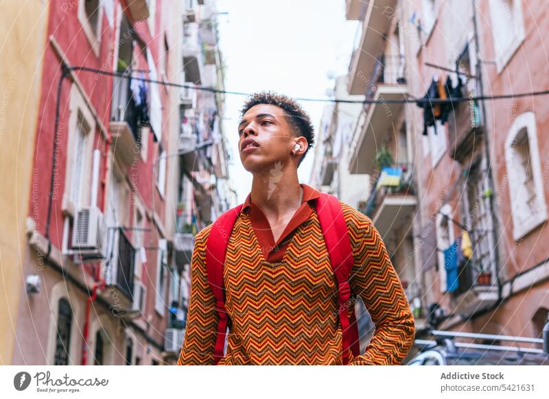 Stylish ethnic man walking on city street style traveler urban earbuds confident listen trendy explore male young hispanic tourist vacation lifestyle colorful