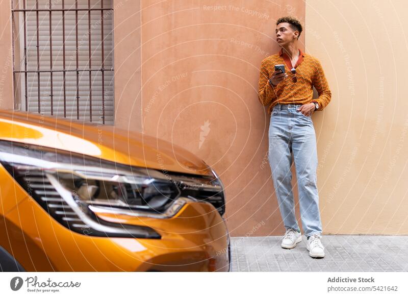 Ethnic man with smartphone standing near modern car style color urban orange automobile using young male ethnic trendy browsing lifestyle gadget hipster online