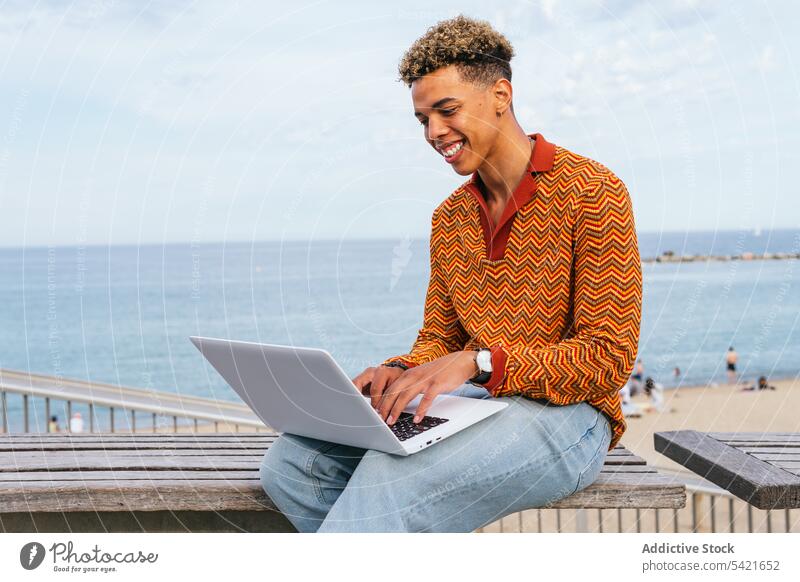 Cheerful young man using laptop on beach happy student freelance style sea typing positive ethnic trendy smile afro curly hair male modern cheerful work remote