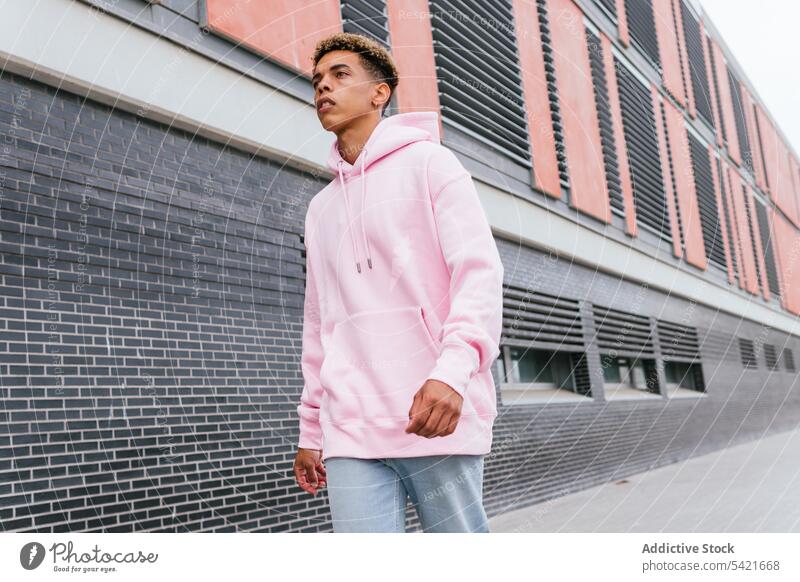 Hipster ethnic man in hoodie walking on street style hipster pink trendy urban modern color outfit young afro dyed hair confident millennial male serious