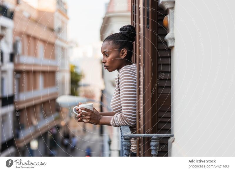 Black woman with coffee contemplating town from balcony reflective wistful hot drink thoughtful lonely house contemplate alone african american black ethnic