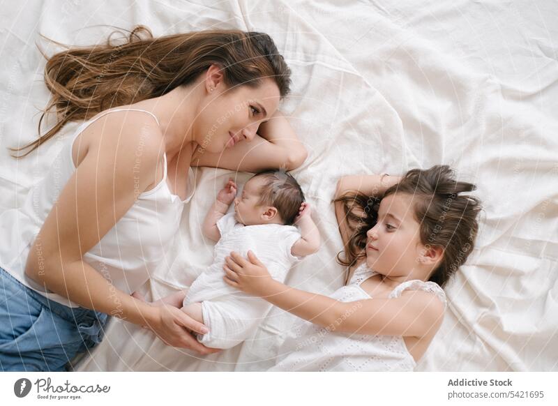 Mother with daughter and newborn lying on bed mother children together tender infant baby kid parent cute happy love little motherhood innocent woman adorable